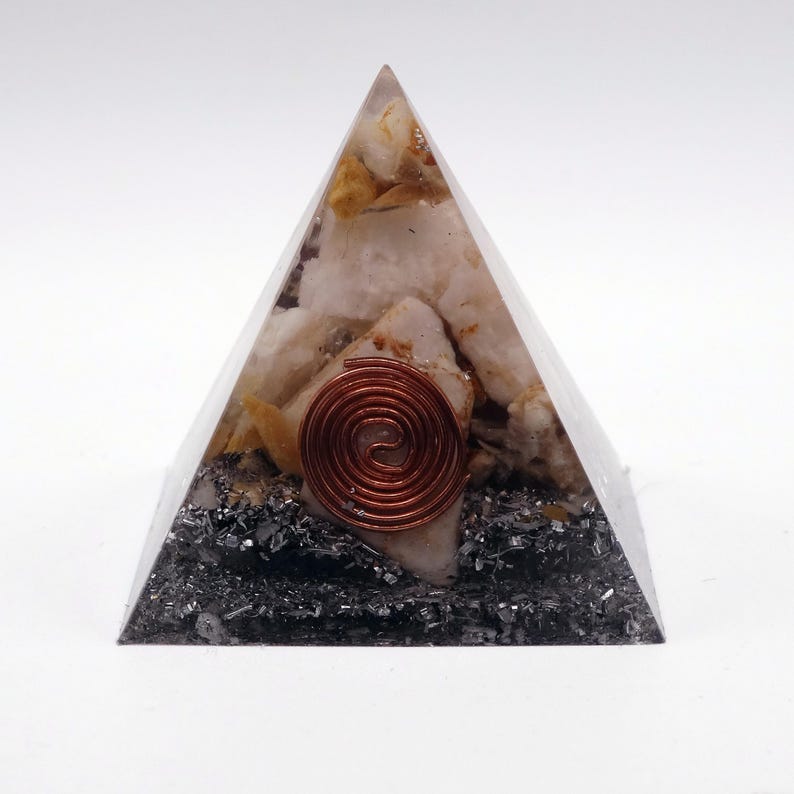 May include: A clear pyramid-shaped orgone energy generator. The pyramid contains white and yellow crystals, dark gray minerals, and a copper coil. The pyramid is on a white background.