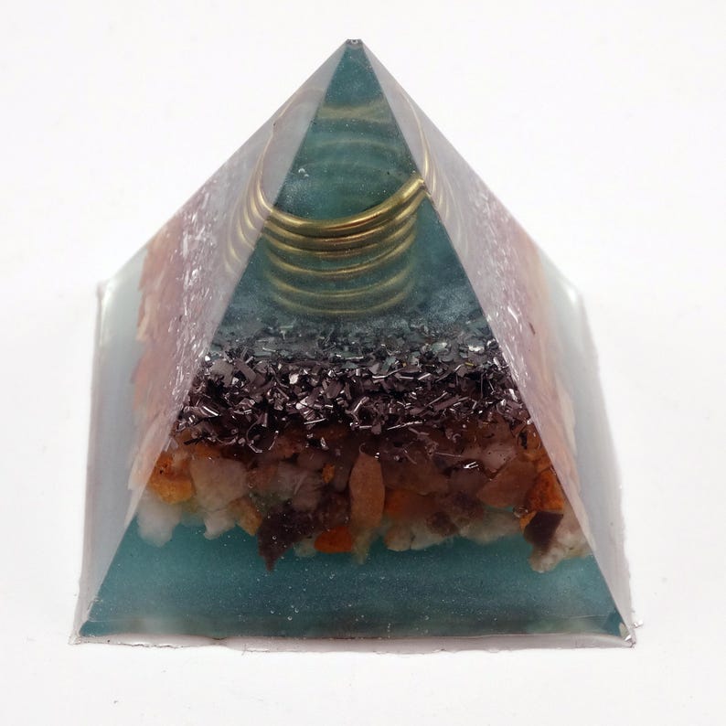 May include: An orgone energy pyramid, constructed from clear resin. The pyramid features layers of blue, brown, and black materials. A set of gold-coloured rings are embedded near the apex.