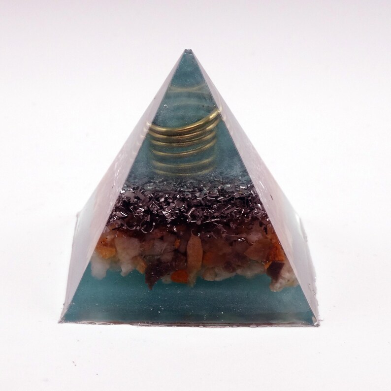 May include: A teal resin pyramid with a gold coil at the top. The pyramid contains layers of dark, black, and orange-brown stones. The pyramid is a decorative item.