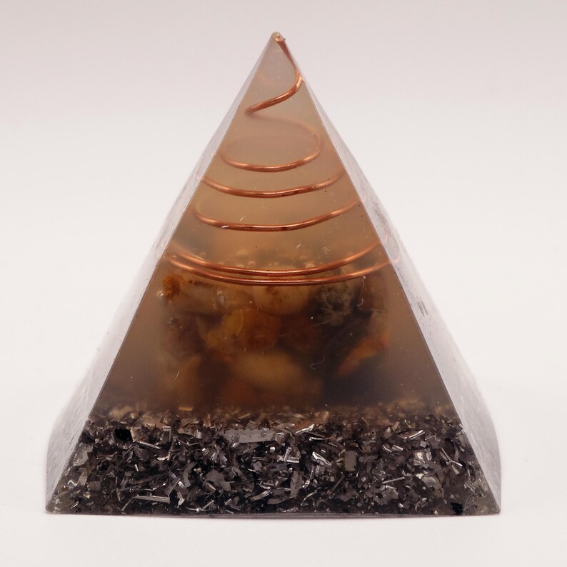 May include: A transparent pyramid-shaped object with a copper coil at the top and embedded stones. The base is filled with dark, shiny fragments. The pyramid is a decorative item, possibly for spiritual or aesthetic purposes.