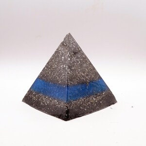 Peut inclure: Un objet d&eacute;coratif en forme de pyramide avec un ext&eacute;rieur mouchet&eacute; gris fonc&eacute; et argent&eacute;. Une bande bleue horizontale est visible au centre. La pyramide est pos&eacute;e sur un fond blanc.