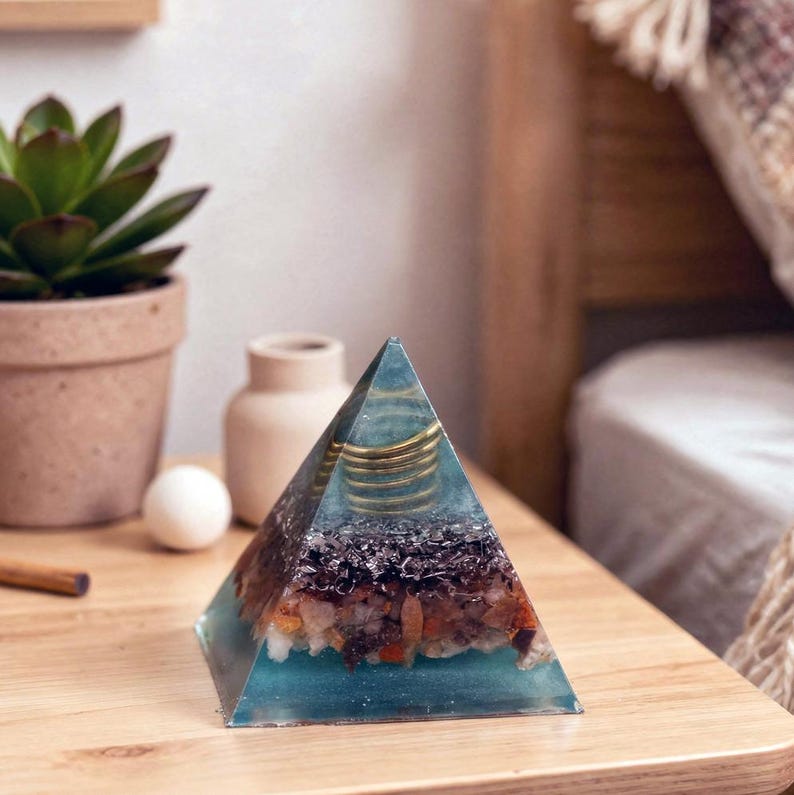 Puede incluir: Una pieza de arte de resina transparente en forma de pirámide con cristales incrustados y espirales doradas. La pirámide tiene un tono azul-verdoso y se encuentra sobre una superficie de madera. Es un objeto decorativo.