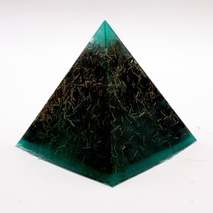 May include: A teal and black pyramid-shaped resin art piece. The pyramid has a teal-colored base and edges, with a dark interior filled with gold-colored, straw-like inclusions. The pyramid is displayed on a white surface.