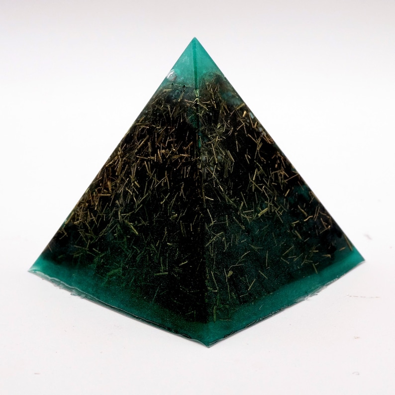 May include: A teal and black pyramid-shaped resin art piece. The pyramid has a teal-colored base and edges, with a dark interior filled with gold-colored, straw-like inclusions. The pyramid is displayed on a white surface.