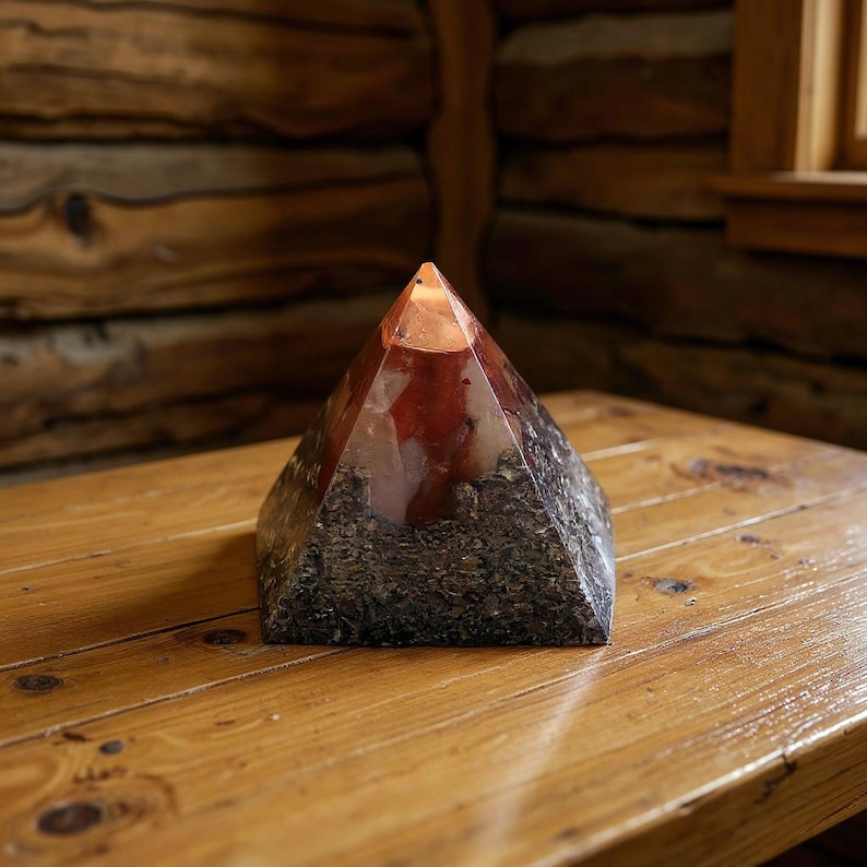 Op de afbeelding: Een piramidevormig decoratief object met een heldere, facetgeslepen top en een roodbruin interieur. De basis is gemaakt van een donker, getextureerd materiaal, mogelijk gedroogde kruiden. Het staat op een houten oppervlak.