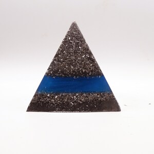 Peut inclure: Une pi&egrave;ce d'art triangulaire en r&eacute;sine avec une fine bande bleue. La forme pyramidale est remplie de petits fragments m&eacute;talliques gris fonc&eacute;. La bande bleue est centr&eacute;e horizontalement sur la pyramide.