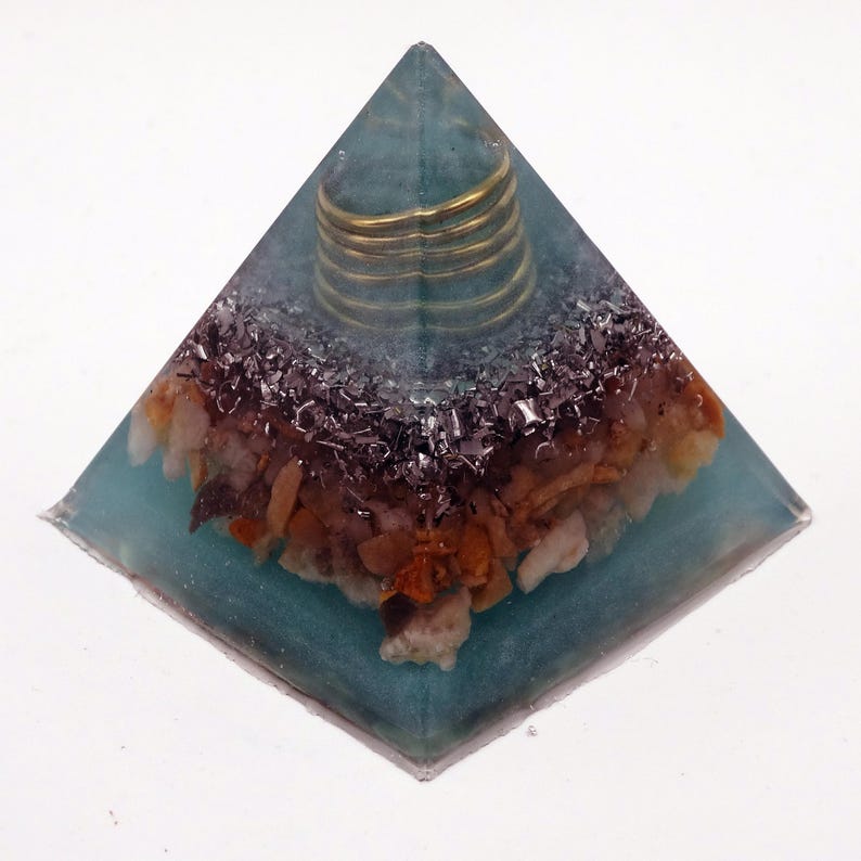 May include: A teal resin pyramid sculpture. It has a gold-coloured coil at the apex, with a mix of brown, beige, and silver-coloured stones and metal fragments embedded within the resin. The base is square.