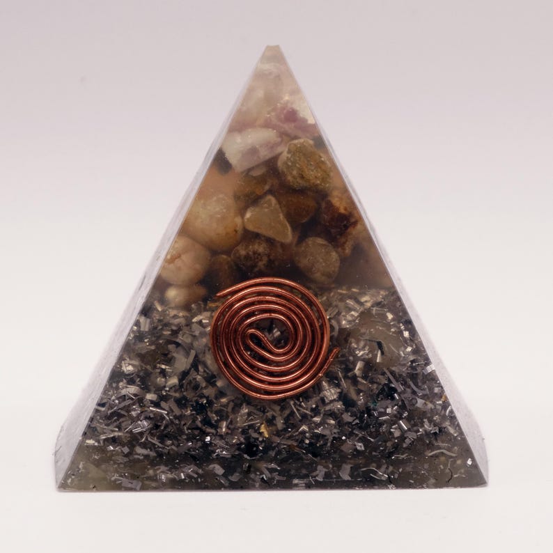 Puede incluir: Una escultura de resina transparente en forma de pir&aacute;mide con piedras incrustadas y una espiral de cobre. La pir&aacute;mide presenta una mezcla de piedras beige, marrones y grises, con una espiral de cobre en el centro.