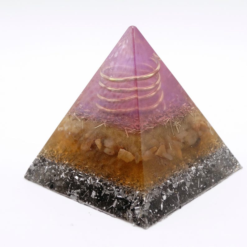 May include: A layered pyramid-shaped object with a purple top, a golden spiral, and a base of black and silver fragments. The middle section is amber-colored with embedded stones. The pyramid is a decorative item.