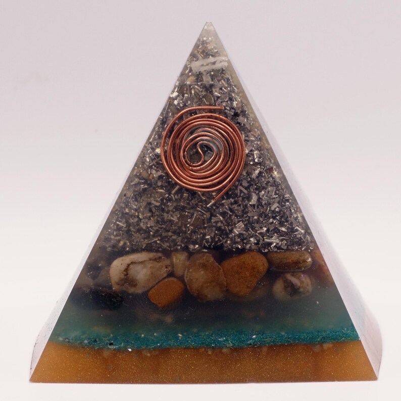 May include: A clear resin pyramid with layers of stones, metal, and a copper coil. The base is a golden color, followed by a teal layer, then a layer of small stones. The top section is filled with metallic fragments, and a copper coil is embedded in the center.