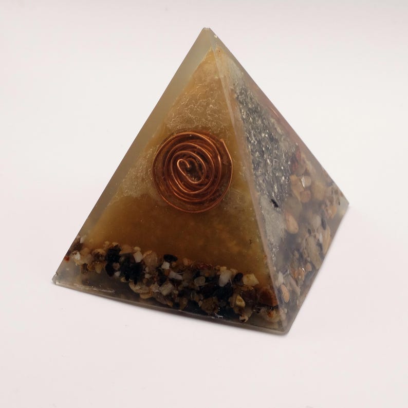 May include: A pyramid-shaped decorative object with a copper spiral embedded in the center. The pyramid is made of a clear resin with a tan and brown interior, and small stones at the base.