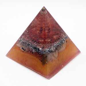 May include: A handcrafted pyramid-shaped decorative object. The pyramid is made of a translucent amber-colored resin, with embedded metal and copper wire elements. A copper coil sits at the top of the pyramid.