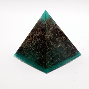 May include: A pyramid-shaped decorative object with a teal green base and edges. The pyramid's interior is dark with gold-colored inclusions. The object is set against a white background.