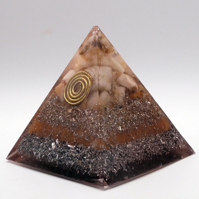 May include: A layered pyramid-shaped object with a clear, glossy exterior. The pyramid features a gold spiral accent and is filled with various materials, including brown, gray, and white elements. The base is dark, transitioning to lighter tones towards the top.