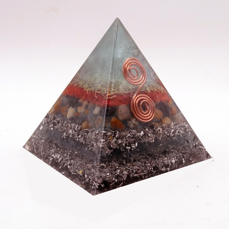 May include: A layered pyramid sculpture with a clear apex and a copper wire spiral. The pyramid's layers include red, brown, and silver materials. The base is a dark, textured material. The pyramid is a decorative item.