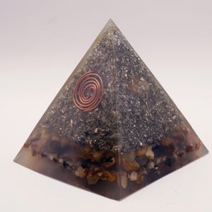 Puede incluir: Pir&aacute;mide de energ&iacute;a org&oacute;nica. Hecha de resina transparente con piedras y escamas met&aacute;licas incrustadas. Una espiral de cobre se encuentra en el centro. La base contiene peque&ntilde;as piedras redondeadas.