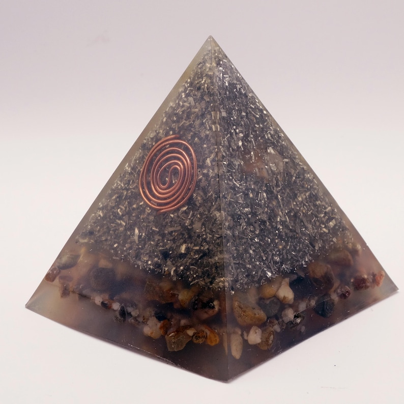 Puede incluir: Pir&aacute;mide de energ&iacute;a org&oacute;nica. Hecha de resina transparente con piedras y escamas met&aacute;licas incrustadas. Una espiral de cobre se encuentra en el centro. La base contiene peque&ntilde;as piedras redondeadas.