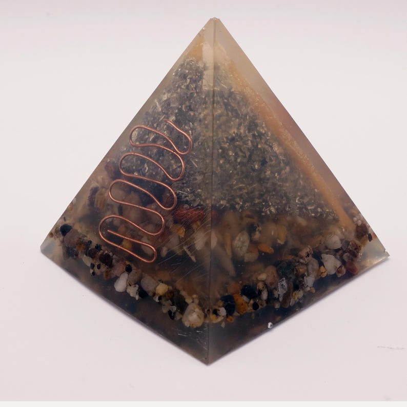 May include: A clear resin pyramid with embedded stones, crystals, and a copper coil. The pyramid has a layered appearance with a mix of colors, including brown, gray, and clear. The copper coil is a prominent feature, adding a decorative element.