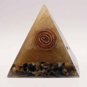 May include: A pyramid-shaped decorative object with a copper coil at the center. The pyramid is a translucent yellow color with small stones at the base. The copper coil is a spiral shape.