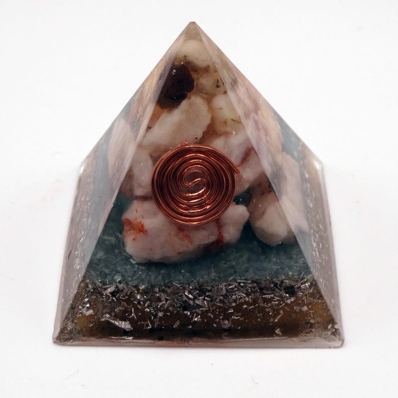 May include: A clear resin pyramid with embedded white and pink stones, a copper coil, and a dark green base. The pyramid shape is a geometric design, with a focus on the internal elements.