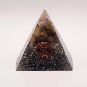 Puede incluir: Una pir&aacute;mide de energ&iacute;a org&oacute;nica. Es transparente y contiene una espiral de cobre y piedras. La pir&aacute;mide est&aacute; sobre un fondo blanco.