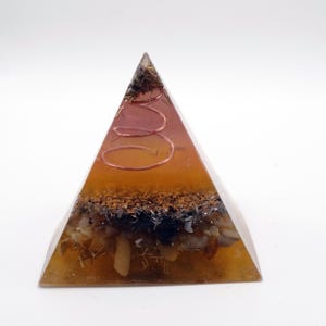 Peut inclure: Une pyramide transparente de couleur ambre, avec des pierres incrust&eacute;es, des particules sombres et une spirale en cuivre. La base de la pyramide est remplie d'un m&eacute;lange de mat&eacute;riaux. Objet d&eacute;coratif.