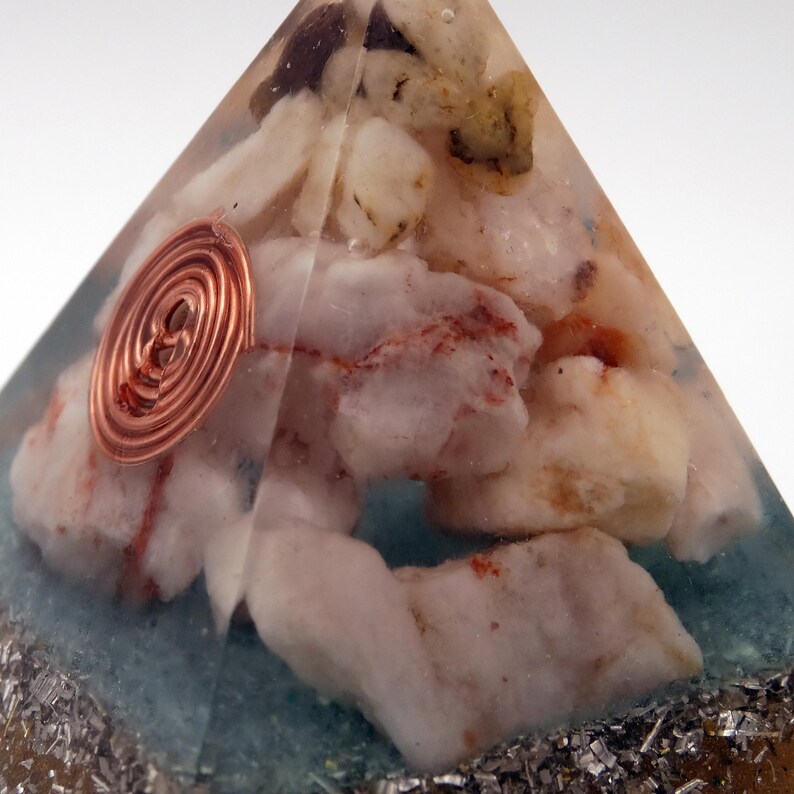 May include: A clear pyramid-shaped resin object with white and beige stones inside. A copper coil is embedded on the side. The base has a blue-green hue with silver-colored flakes at the bottom.