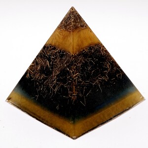 Puede incluir: Un objeto decorativo en forma de pir&aacute;mide con un dise&ntilde;o en capas. La base es de color azul oscuro y dorado, pasando a negro en el medio y dorado en la parte superior. La pir&aacute;mide est&aacute; rellena de peque&ntilde;os trozos marrones en forma de paja.