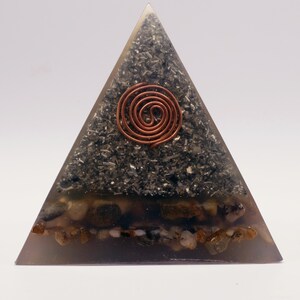 Puede incluir: Un generador de energ&iacute;a org&oacute;nica en forma de pir&aacute;mide. La pir&aacute;mide est&aacute; hecha de resina transparente con un interior gris oscuro lleno de peque&ntilde;as piedras y una espiral de cobre. La base contiene peque&ntilde;as piedras de color marr&oacute;n claro.