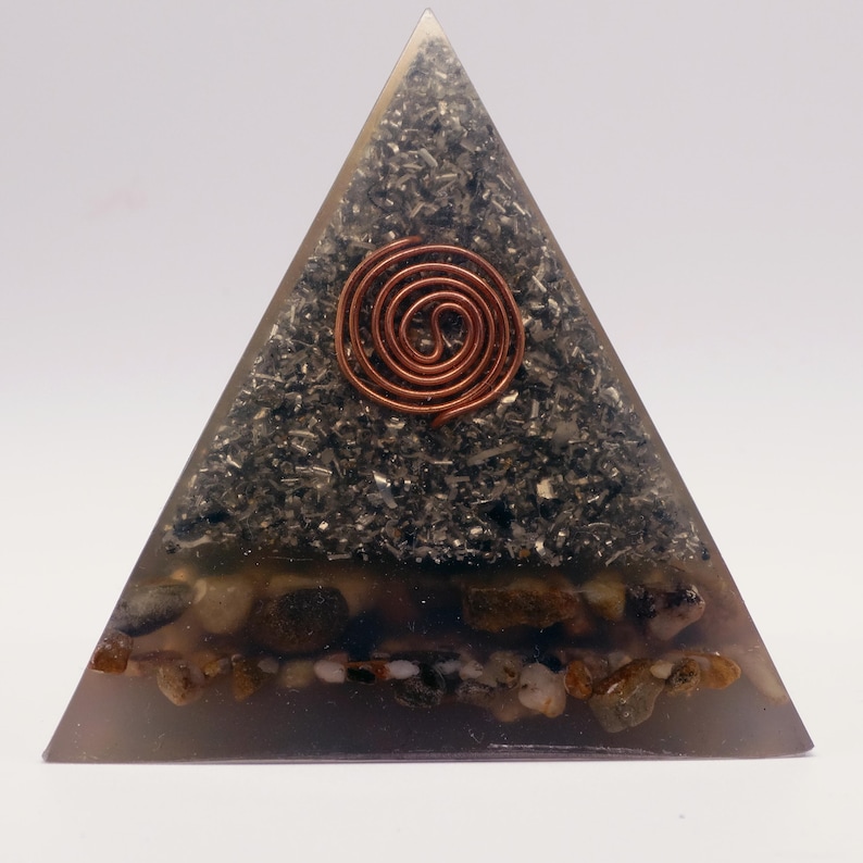 Puede incluir: Un generador de energ&iacute;a org&oacute;nica en forma de pir&aacute;mide. La pir&aacute;mide est&aacute; hecha de resina transparente con un interior gris oscuro lleno de peque&ntilde;as piedras y una espiral de cobre. La base contiene peque&ntilde;as piedras de color marr&oacute;n claro.