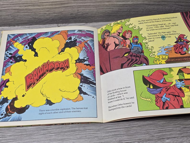 Puede incluir: Ilustraci&oacute;n de un libro abierto, con vi&ntilde;etas de c&oacute;mic. Un panel muestra una explosi&oacute;n amarilla con la palabra "BAWHOOOM". Otros paneles representan a He-Man y sus amigos, y a Orko. El texto incluye di&aacute;logos y narrativa.