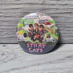 May include: Round button featuring a graphic of the Stray Cats band in a hot rod. The button has a blue and green background with text that reads "Stray Cats" and other text including "18 Miles to Memphis".