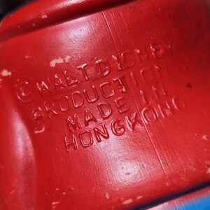 May include: Close-up of a red plastic toy with embossed text. The text reads "&copy; WALT DISNEY PRODUCTION MADE IN HONGKONG". The toy has a blue section visible at the bottom.