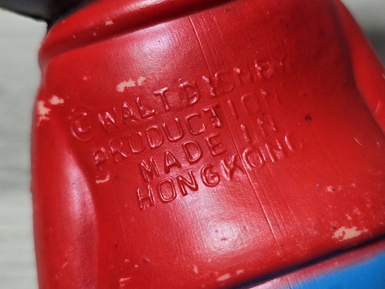 May include: Close-up of a red plastic toy with embossed text. The text reads "&copy; WALT DISNEY PRODUCTION MADE IN HONGKONG". The toy has a blue section visible at the bottom.