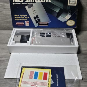 May include: A Nintendo NES Satellite remote control module in its original packaging. The box features the text NES SATELLITE, Remote Control Module, and Up to 4-player action with A&B Turbo Control. Includes the device, styrofoam, and manual.