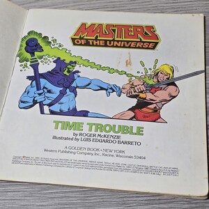Puede incluir: Un libro dorado vintage de "Masters of the Universe" titulado "Time Trouble". La portada presenta ilustraciones de Skeletor y He-Man en acci&oacute;n, con el logotipo de la serie en la parte superior. El libro es de Western Publishing.
