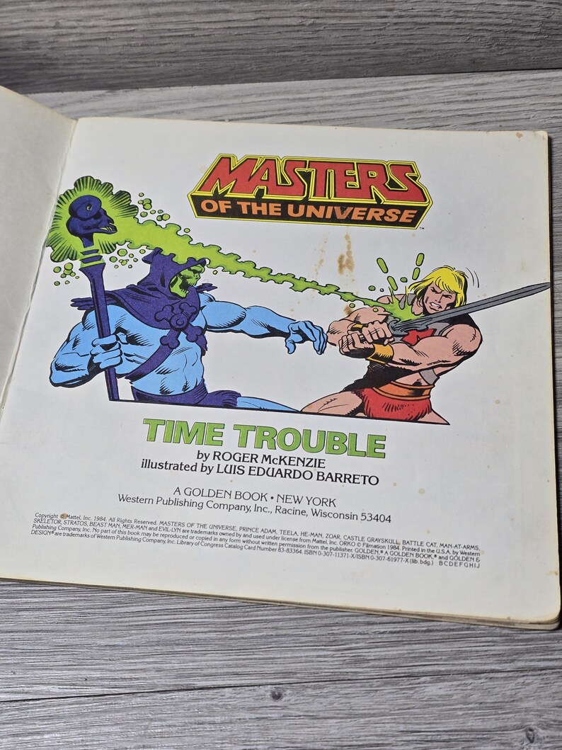 Puede incluir: Un libro dorado vintage de "Masters of the Universe" titulado "Time Trouble". La portada presenta ilustraciones de Skeletor y He-Man en acci&oacute;n, con el logotipo de la serie en la parte superior. El libro es de Western Publishing.