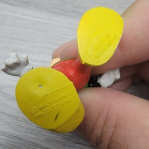 Pode incluir: Figurinha de pl&aacute;stico amarela de um personagem de desenho animado com roupas vermelhas, verdes e brancas. A figurinha tem uma base amarela com o texto "&copy; WALT DISNEY PRODUCTIONS" na parte inferior.