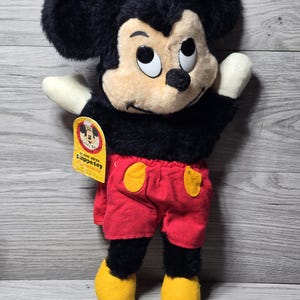 May include: A black and red Mickey Mouse puppet with a yellow tag that says "come alive puppet" and "authentic disney".