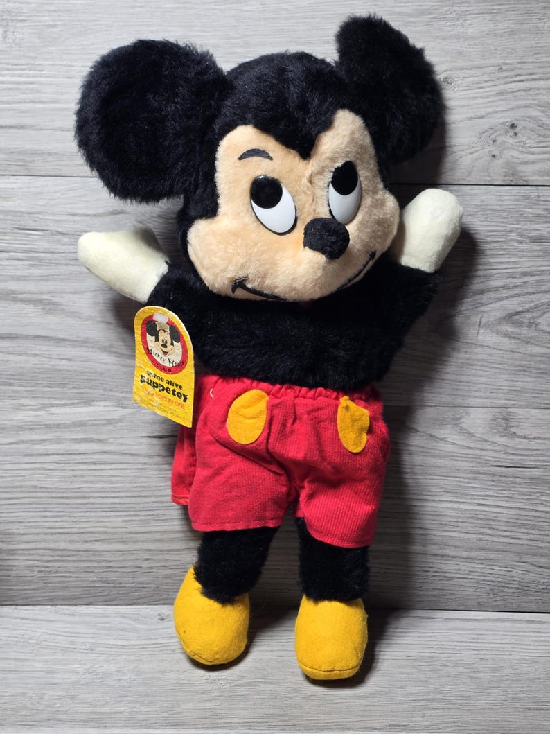 May include: A black and red Mickey Mouse puppet with a yellow tag that says "come alive puppet" and "authentic disney".
