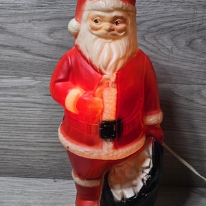 May include: A vintage Santa Claus figure, with a red suit, hat, and white beard. The figure holds a sack and has an internal light. The plastic figure is a Christmas decoration, designed to be illuminated.