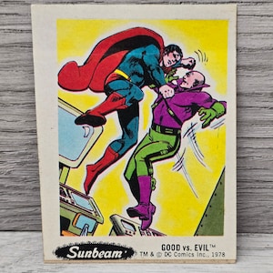 Op de afbeelding: Een vintage Sunbeam-verzamelkaart met Superman in een rode cape en een blauw pak dat vecht tegen Lex Luthor in een paars pak en een groene cape. De kaart heeft de tekst "GOOD vs. EVIL" en "TM & © DC Comics Inc., 1978".
