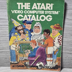Puede incluir: Catálogo vintage de Atari Video Computer System. La portada verde presenta el título en blanco y una colorida ilustración de personajes de dibujos animados. El catálogo presenta el texto "43 Game Program Cartridges."