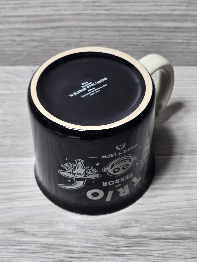 Puede incluir: Taza de cer&aacute;mica negra con asa y borde blancos, con personajes de "Pesadilla antes de Navidad". El dise&ntilde;o incluye las palabras "RIO OF TERROR" y "Oogie's Crew."