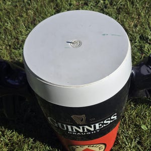 May include: A black and red insulated cooler shaped like a pint glass with the Guinness logo and the text "Draught". The cooler has a white lid with a small hole in the center.