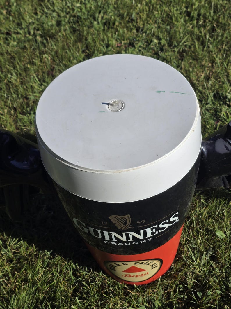 May include: A black and red insulated cooler shaped like a pint glass with the Guinness logo and the text "Draught". The cooler has a white lid with a small hole in the center.