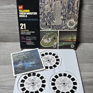 May include: A vintage GAF Talking View-Master Reels set, 'New York City Sight-Seeing Tour'. The box displays a cityscape and the Statue of Liberty. Includes 3 reels and a booklet. The set is presented in a white plastic tray.