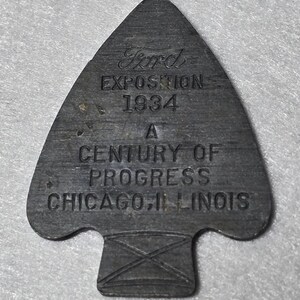 Könnte beinhalten: Ein Pfeilspitzenförmiges Metall-Souvenir von der Ford Exposition 1934, einem Jahrhundert des Fortschritts in Chicago, Illinois. Das graue Metallstück hat geprägten Text und einen dekorativen Sockel.