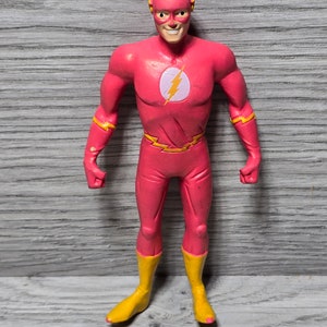 May include: A red and yellow plastic action figure of The Flash, a superhero with super speed. The figure is posed with arms outstretched and a slight smile on its face.