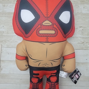 Puede incluir: Juguete de peluche rojo y negro de Deadpool con una máscara de lucha libre y un atuendo de lucha libre rojo y negro. El juguete está de pie sobre una superficie de madera. El juguete tiene una etiqueta que dice "Marvel" y "Deadpool".